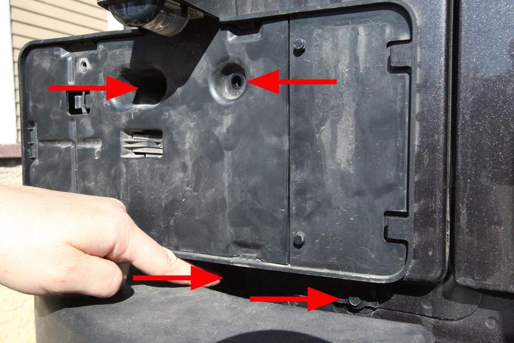 Remove four license plate frame bolts using a 7 mm socket, extension bar, and socket