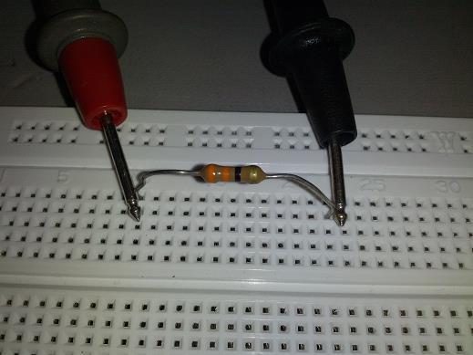 If both leads are in the same set and the same column, the test current being generated by the DMM will go through the bread board wiring instead of the resistor because it has less