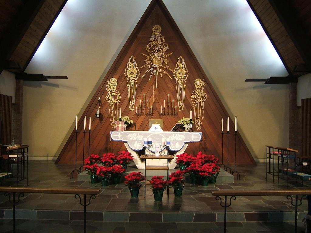 Christmas tells us Christ is Here White Poinsettias on reredos 24 red poinsettias around Altar and front entry and Baptismal font.