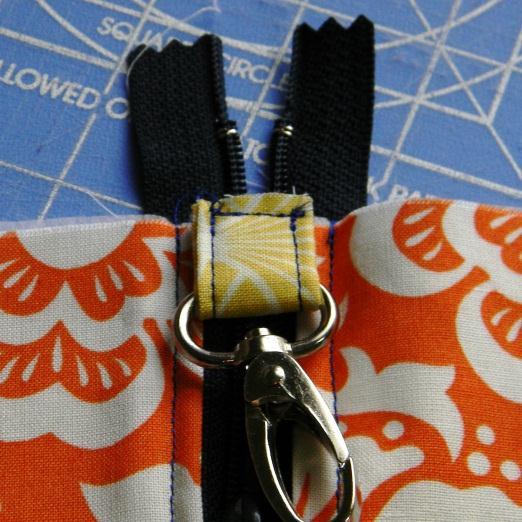 With the zipper closed (but within the fabric pieces as shown) place the tab with the attached clasp at the end with the